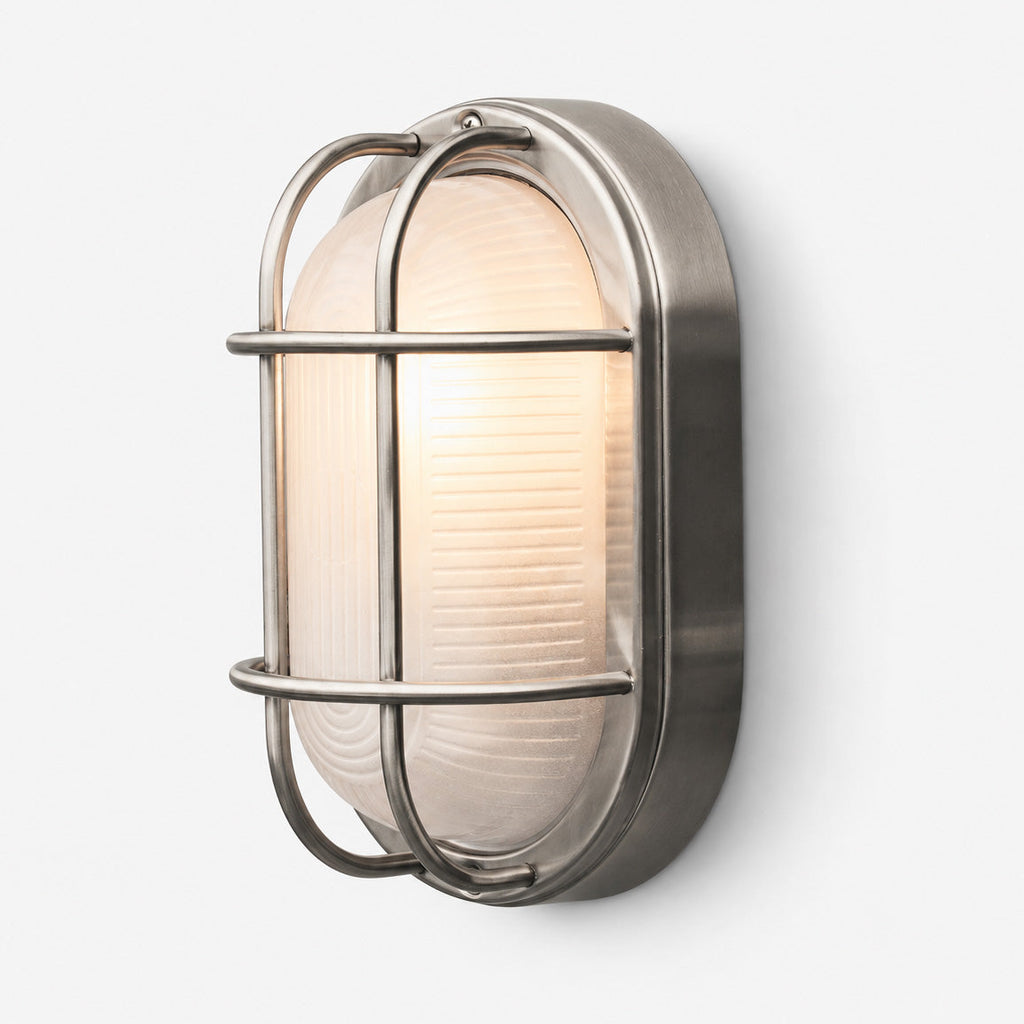 A modern industrial wall sconce with a brushed silver metal frame and a warm white ribbed glass shade, shown mounted on a light gray wall.