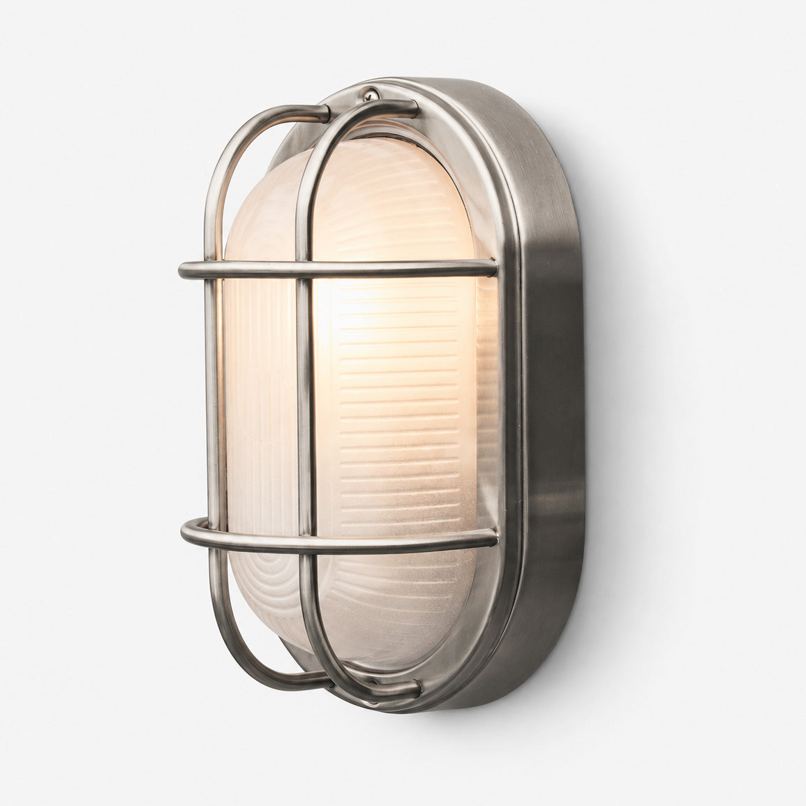 A modern industrial wall sconce with a brushed silver metal frame and a warm white ribbed glass shade, shown mounted on a light gray wall.