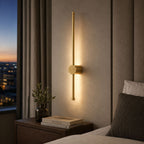 Vireo brushed gold LED stick wall light lit beside a bed at night