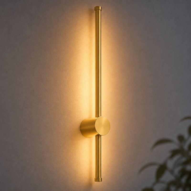 Vireo brushed gold LED stick wall light with ambient backlight glowing on a wall