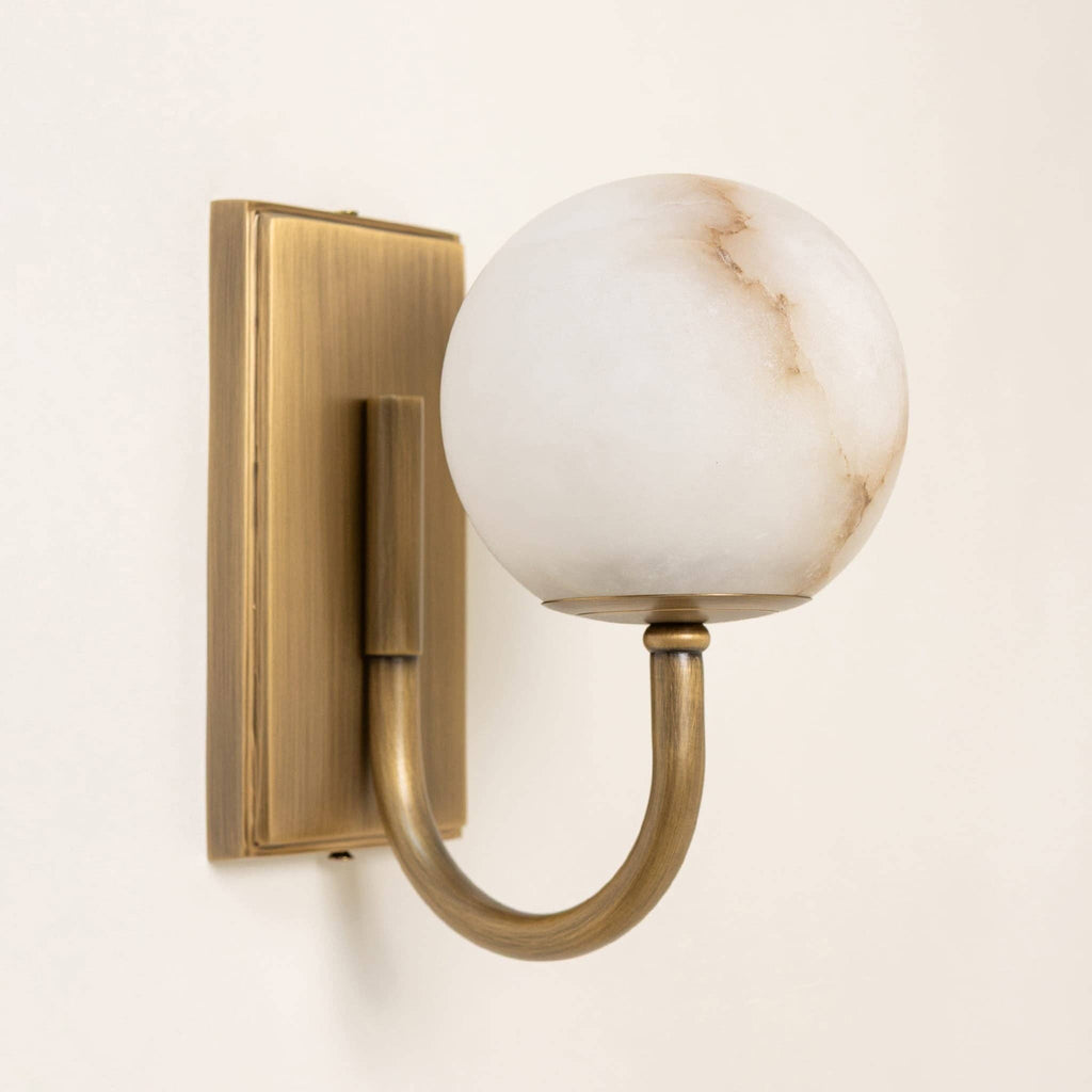 Alabaster globe wall light with antique brass fixture casting warm glow