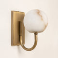 Alabaster globe wall light with antique brass fixture casting warm glow