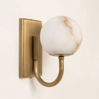 Alabaster globe wall light with antique brass fixture casting warm glow