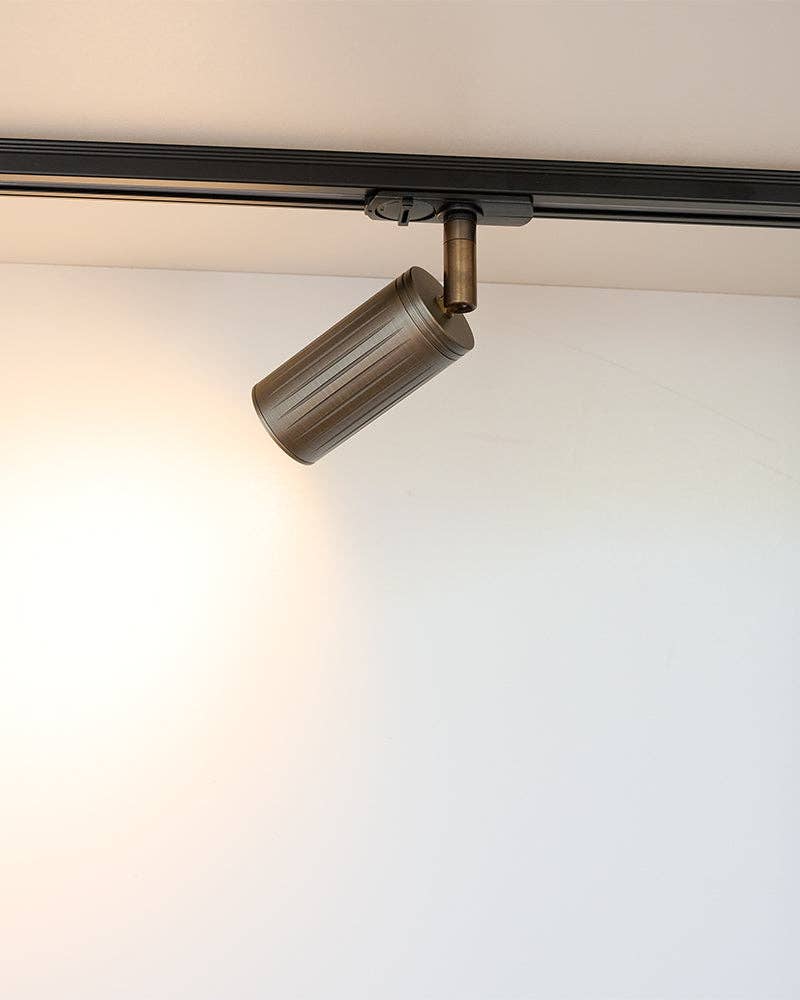 Close up of browned brass track light showing warm metallic patina