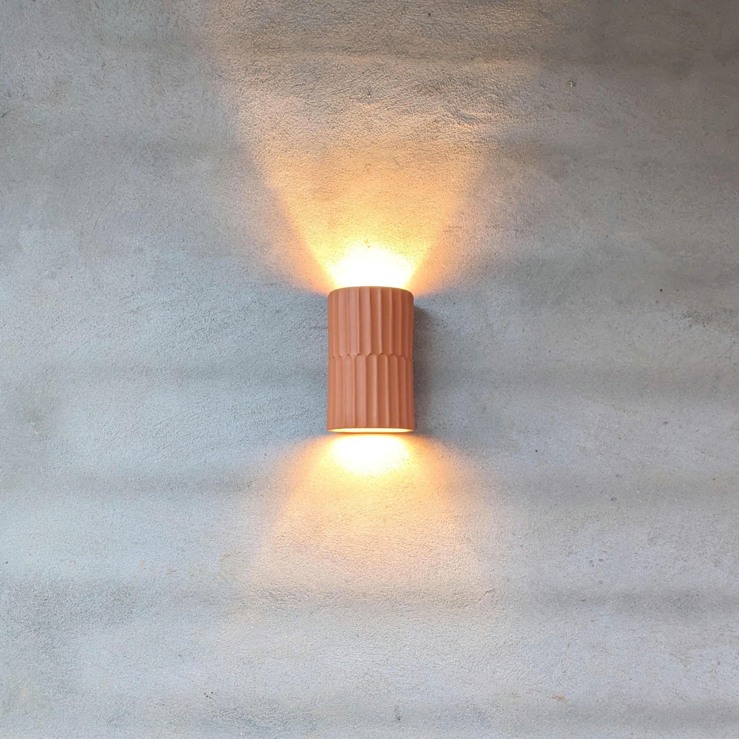 Handmade Portuguese wall light in warm terracotta creating soft shadow patterns