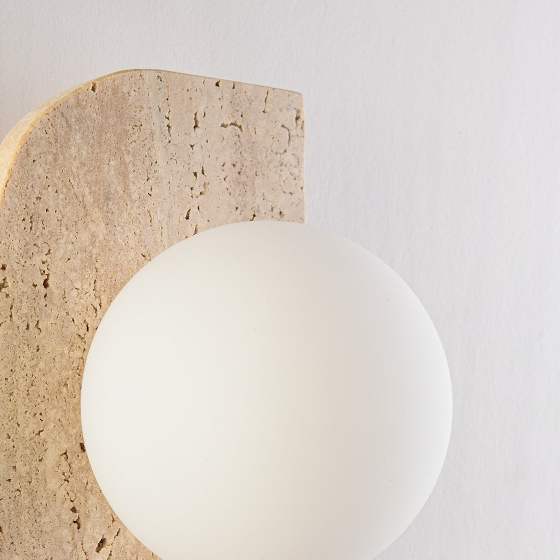 Close up of travertine stone backplate and opal glass globe on Orla wall light