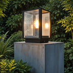 Black outdoor post lantern illuminated in garden pathway setting