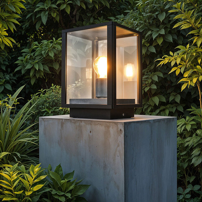 Black outdoor post lantern illuminated in garden pathway setting
