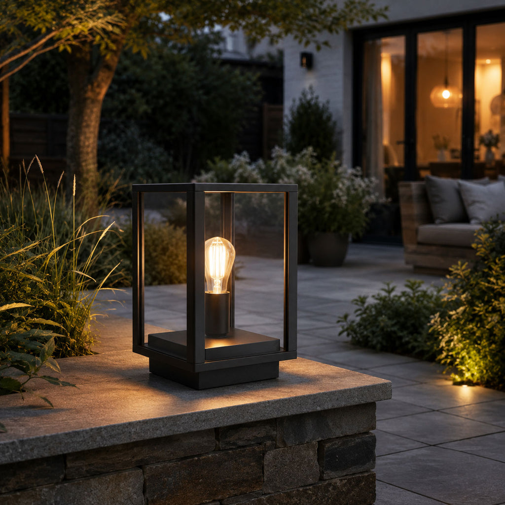 Sem black glass panel lantern lit on a garden wall beside an outdoor sofa at night