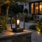 Sem black glass panel lantern lit on a garden wall beside an outdoor sofa at night