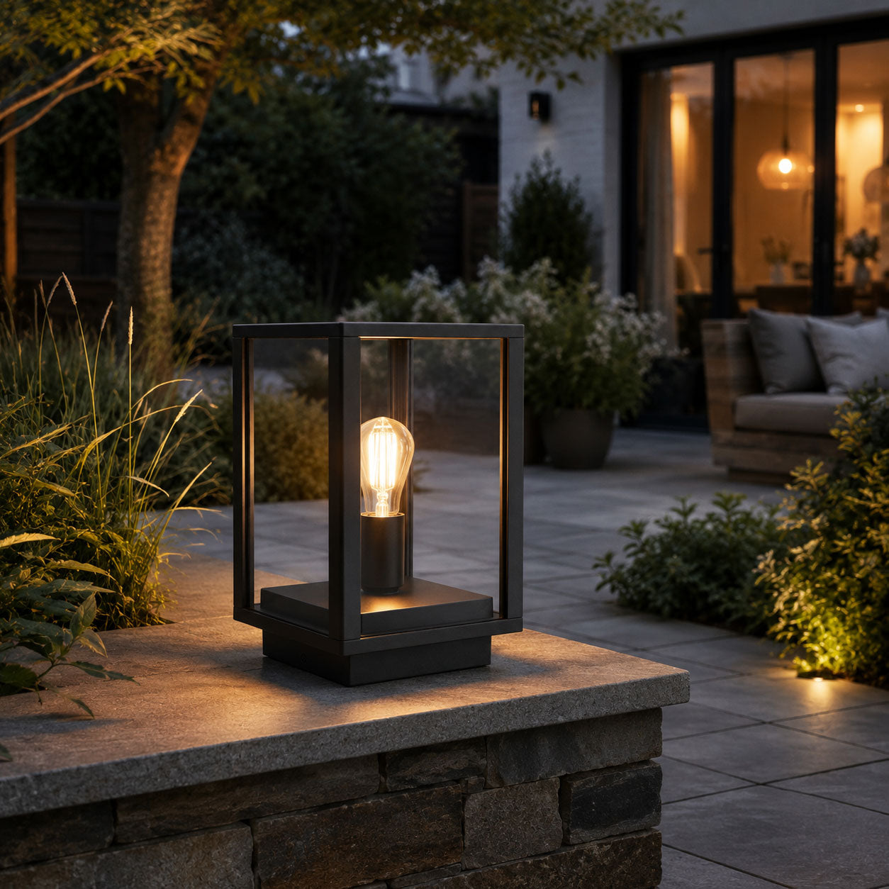 Sem black glass panel lantern lit on a garden wall beside an outdoor sofa at night