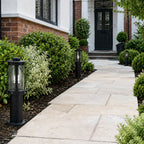 Lucia 40cm black bollard post light beside a paved path and box hedging in daylight