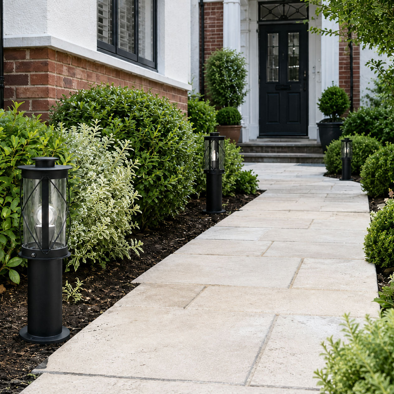 Lucia 40cm black bollard post light beside a paved path and box hedging in daylight