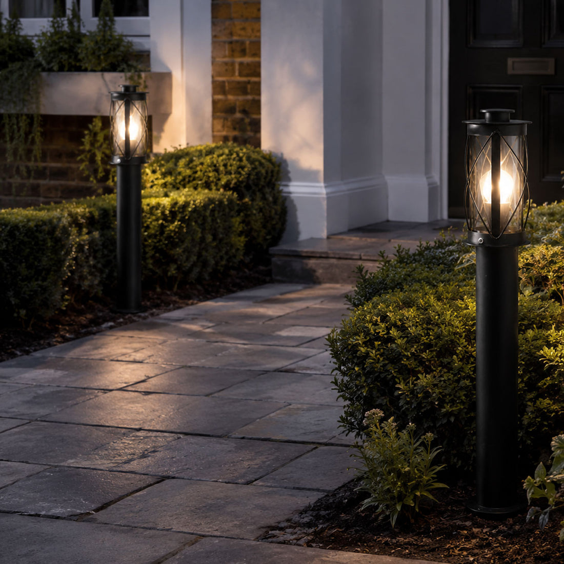 Lucia black bollard post lights lit along a paved front path to a porch at dusk