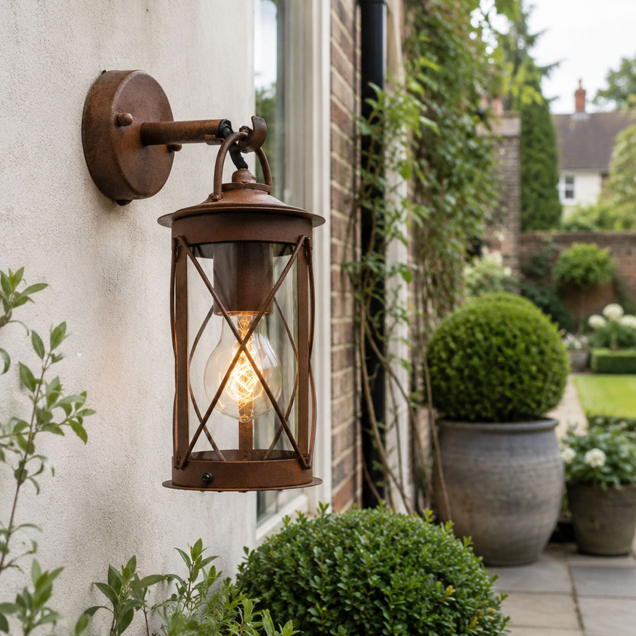 Alicia rustic brown caged wall lantern on a cream rendered wall beside a doorway and topiary