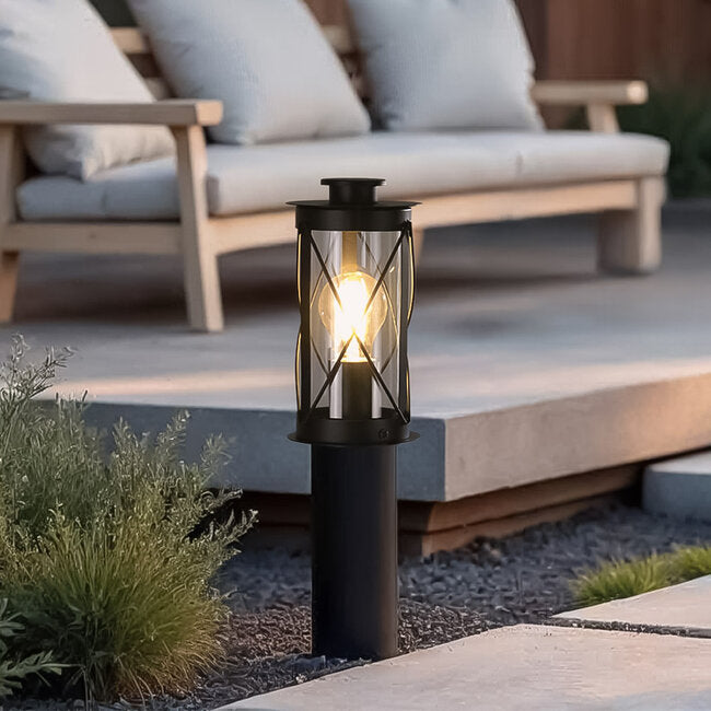 Rustic bollard garden light illuminated along pathway at dusk